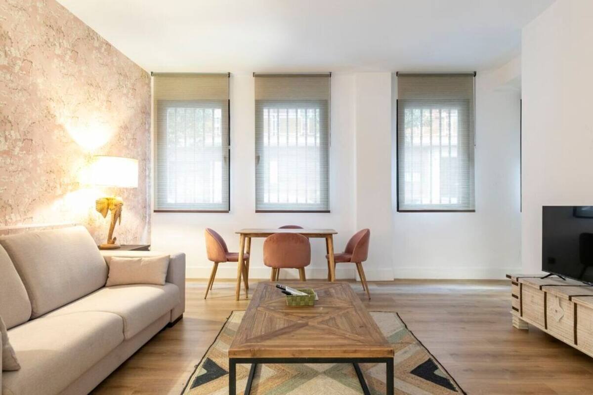 A modern living room with a sofa, a coffee table, a TV, and a dining area with chairs.