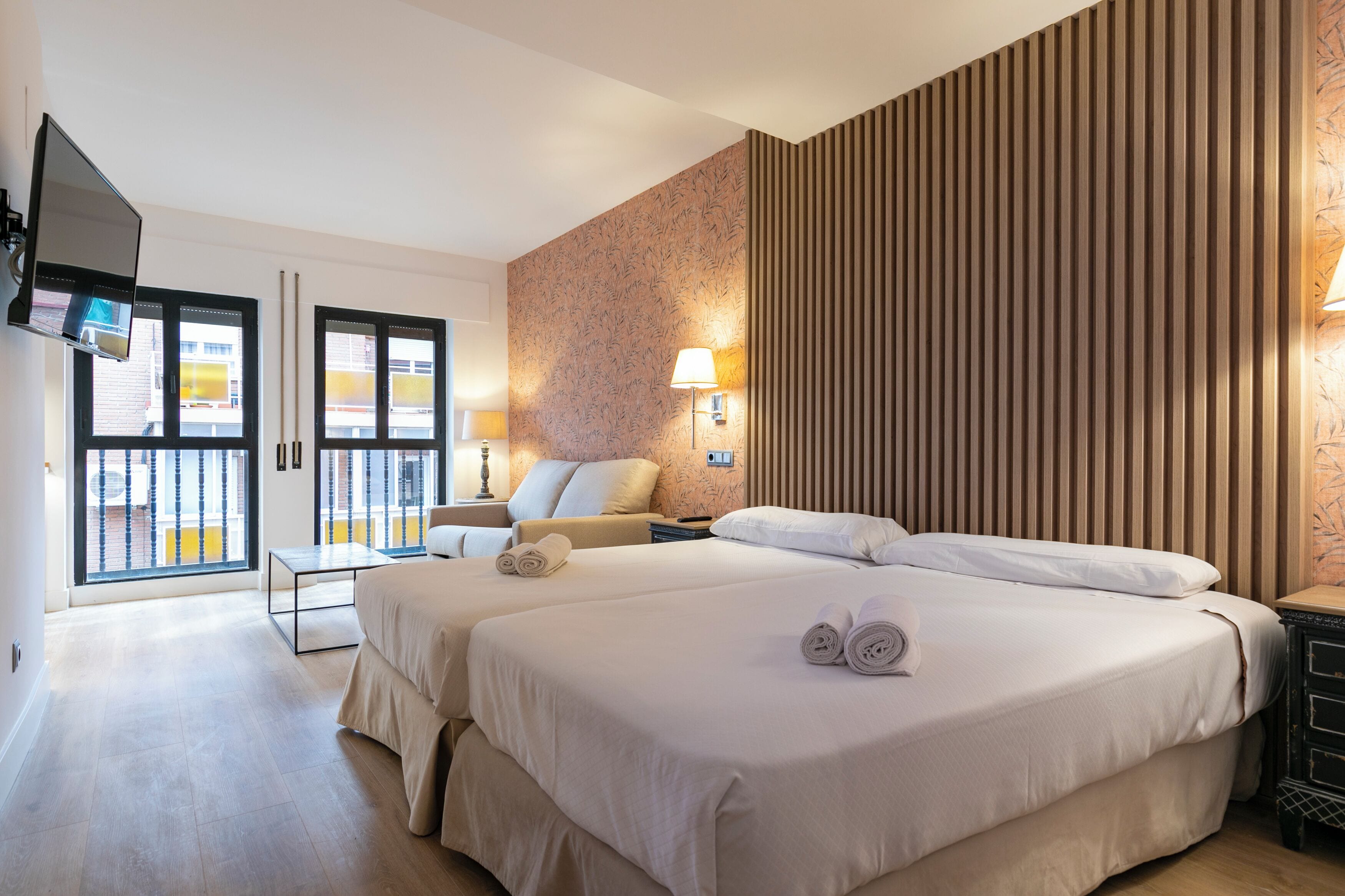 Habitación de hotel con dos camas, televisión, escritorio y balcón con vistas.