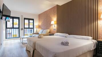Habitación de hotel con dos camas, televisión, escritorio y balcón con vistas.
