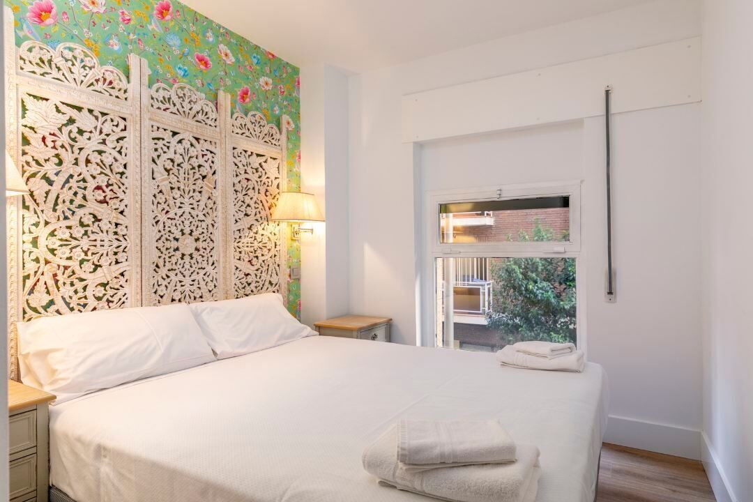 A bedroom with a bed, a nightstand, a window with a view, and a decorative wall panel.