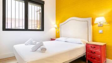 Una habitación de hotel con una cama, dos mesitas de noche, un ventanal y una pared amarilla.