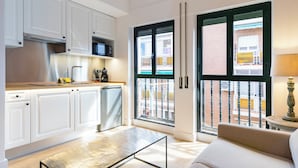 A modern kitchen with white cabinets, a microwave, and a coffee machine. There is a sliding glass door leading to a balcony with a view of buildings.