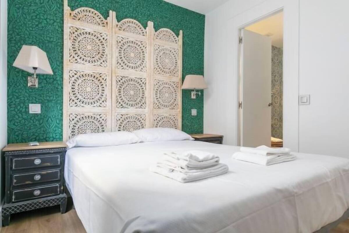 A neatly made bed with white linens, a decorative headboard, and two bedside lamps.