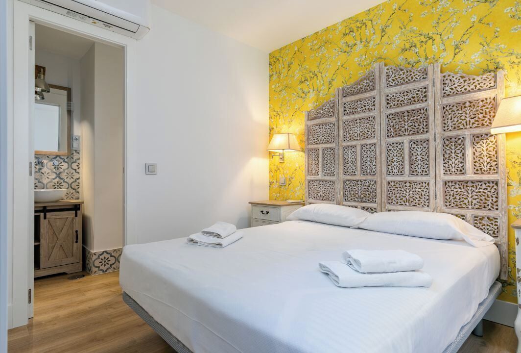 Une chambre d’hôtel avec un lit, une table de chevet, une lampe et une salle de bain visible à travers une porte ouverte.