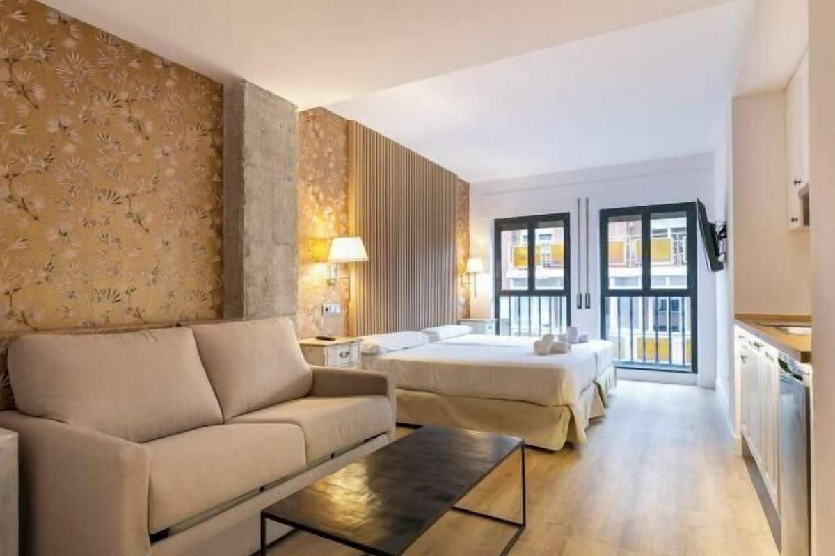 A hotel room with a sofa, two beds, a dining area, and a view of the outside.