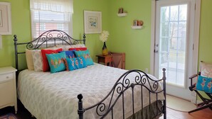 A bedroom with a bed, a nightstand, a chair, a window with blinds, and a door. - Eel Creek Escape -  Water Front  - Water Access - Screened Porch NO LINENS (Chincoteague)