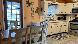 A kitchen with white cabinets, a wooden dining table with chairs, a ceiling fan, and a sign reading "BEACH HOUSE". - Eel Creek Escape -  Water Front  - Water Access - Screened Porch NO LINENS (Chincoteague)