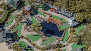 An aerial view of a golf course with multiple holes, a water hazard, and a small building structure. - Please welcome "Two Hands Excited" to the Ocean Lakes rental program. (Myrtle Beach)