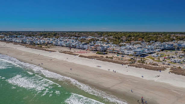 An aerial view of a coastal residential area with beachfront properties, a sandy beach, and a clear blue sky. - Please welcome "Two Hands Excited" to the Ocean Lakes rental program. (Myrtle Beach)