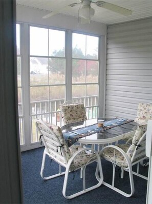 Enjoy a serene atmosphere in this sunroom with a large windowed wall, a round table, and comfortable seating for four.