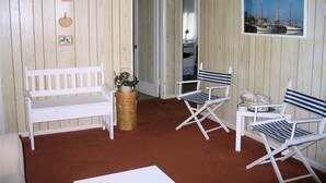 A room with a wooden paneled wall, a white bench, two striped chairs, a wicker basket, and a framed picture of boats. - Sea Pines -2BR  CLOSE TO SHOPPING,SCREENED PORCH, Linens and Towels Provided (Chincoteague)