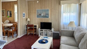 A living room with a ceiling fan, a television, a sofa, a coffee table, and a dining area with chairs and a table. - Sea Pines -2BR  CLOSE TO SHOPPING,SCREENED PORCH, Linens and Towels Provided (Chincoteague)