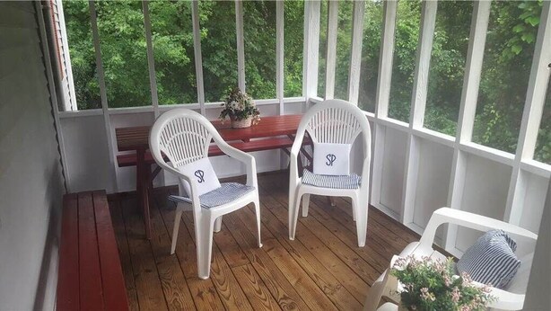 A covered porch with two white plastic chairs, a wooden bench, and a small table with a plant. - Sea Pines -2BR  CLOSE TO SHOPPING,SCREENED PORCH, Linens and Towels Provided (Chincoteague)