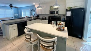 A modern kitchen with white cabinetry, a central island, two bar stools, a microwave, a refrigerator, and pendant lighting. - Josie's Getaway - Pet Friendly -Mini-Vacations and Month to Monthly Available (Chincoteague)