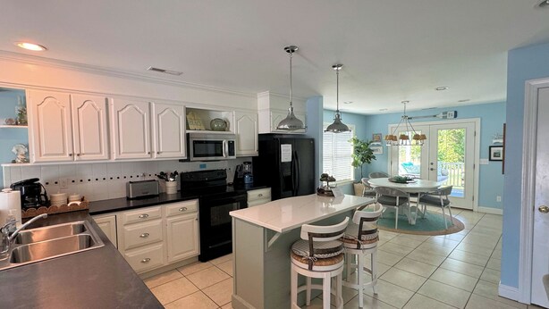 A kitchen with white cabinets, a black refrigerator, a microwave, and a sink. There is a dining area with a table and chairs. - Josie's Getaway - Pet Friendly -Mini-Vacations and Month to Monthly Available (Chincoteague)