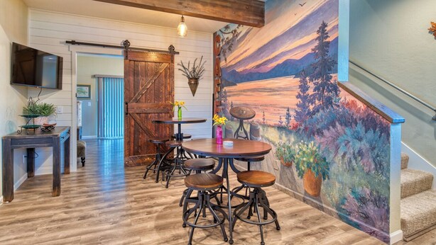 A dining area with a wooden table and chairs, a hanging plant, and a mural on the wall. - A/C LakeAccess GameRoom Xbox DogOK kayaks paddleboards Private30'Dock Sleeps 14 (Sagle)