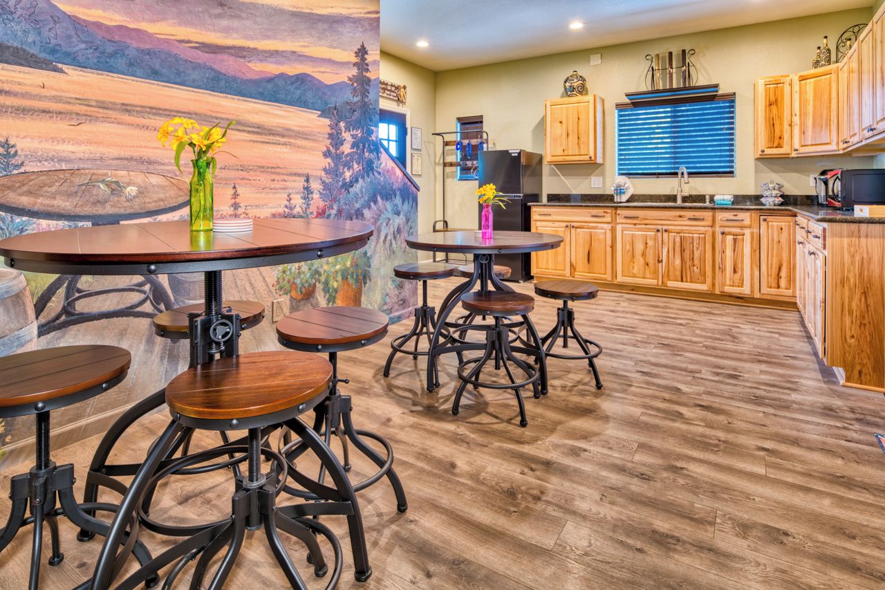 A dining area with round tables and stools, a kitchen with wooden cabinets, and a mural of a landscape on the wall.