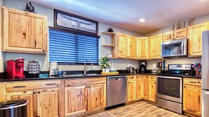 A modern kitchen with wooden cabinets, stainless steel appliances, and a large window with blinds. - A/C LakeAccess GameRoom Xbox DogOK kayaks paddleboards Private30'Dock Sleeps 14 (Sagle)