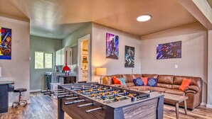 A living room with a foosball table, a brown leather couch, and colorful cushions. - A/C LakeAccess GameRoom Xbox DogOK kayaks paddleboards Private30'Dock Sleeps 14 (Sagle)