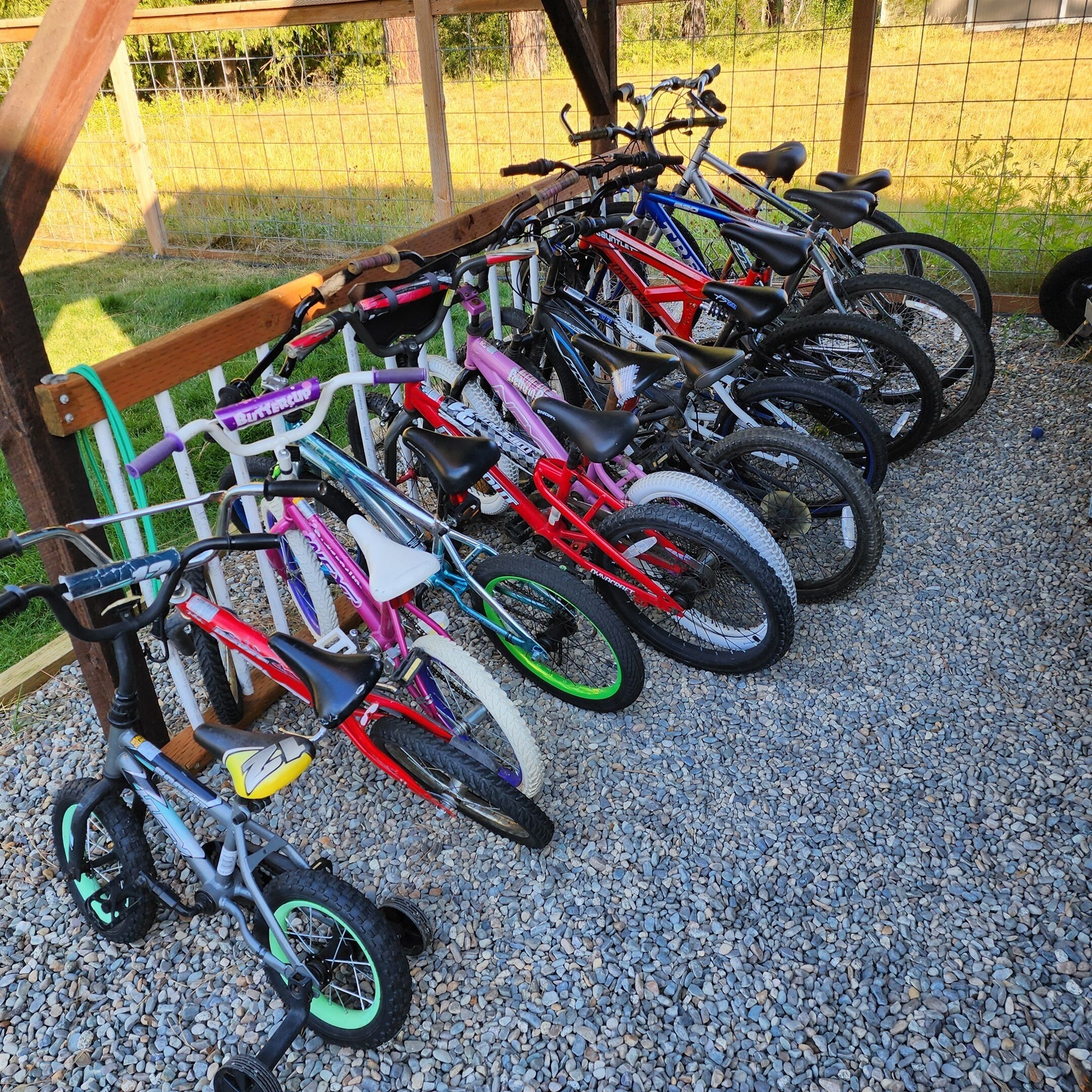 A row of bicycles parked on a gravel surface, leaning against a wooden structure.
