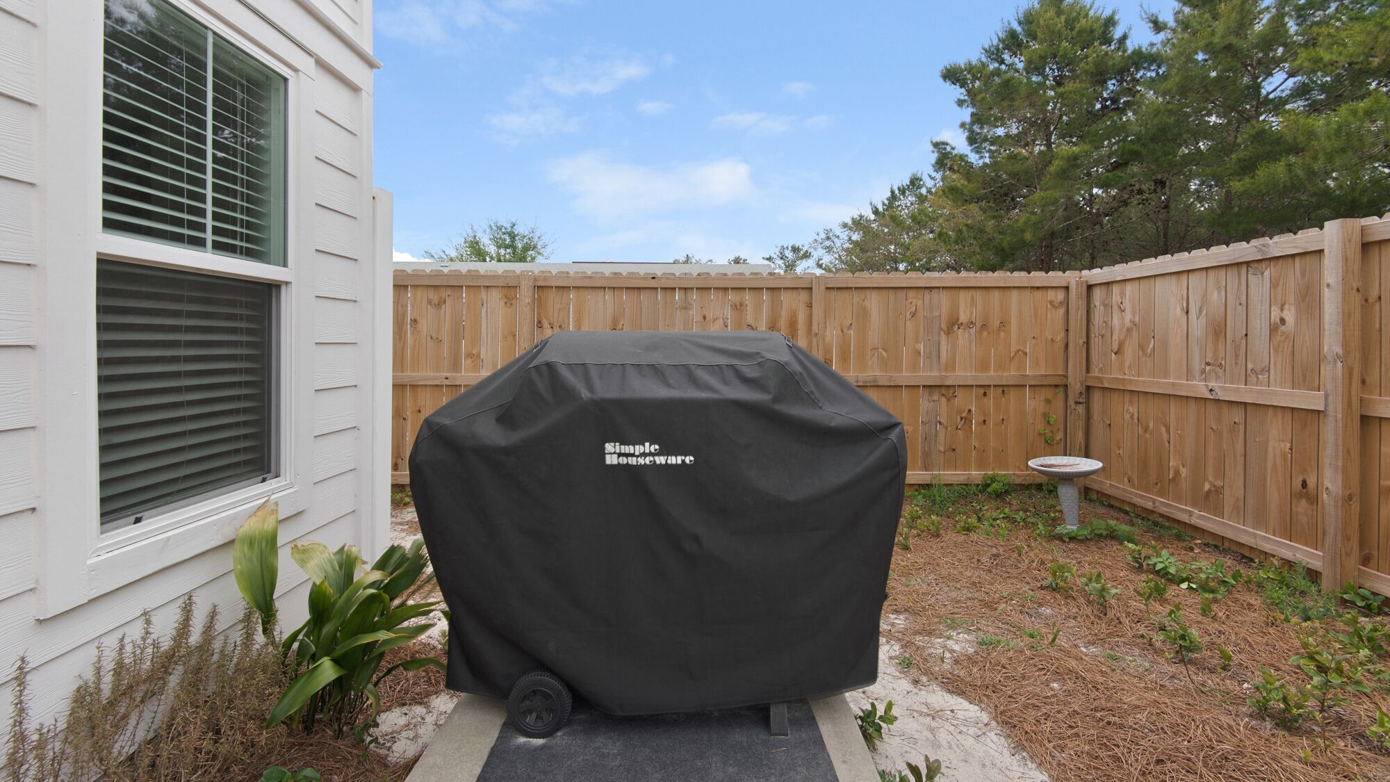 A covered barbecue grill in a backyard with a wooden fence and a bird bath.