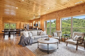 Relax in a spacious living area with a high ceiling, comfortable sofa set, and dining table overlooking a lush landscape.