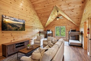 Cozy cabin-style interior with a high ceiling, sofa, armchairs, and a large window.