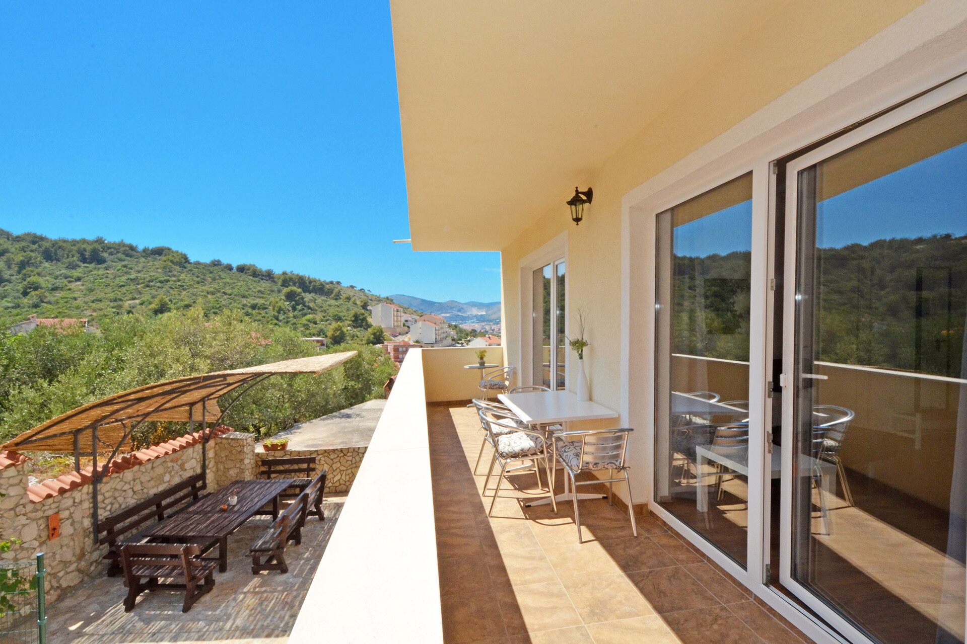 Uma varanda com mesa e cadeiras, um banco de madeira e vista para uma encosta verde.
