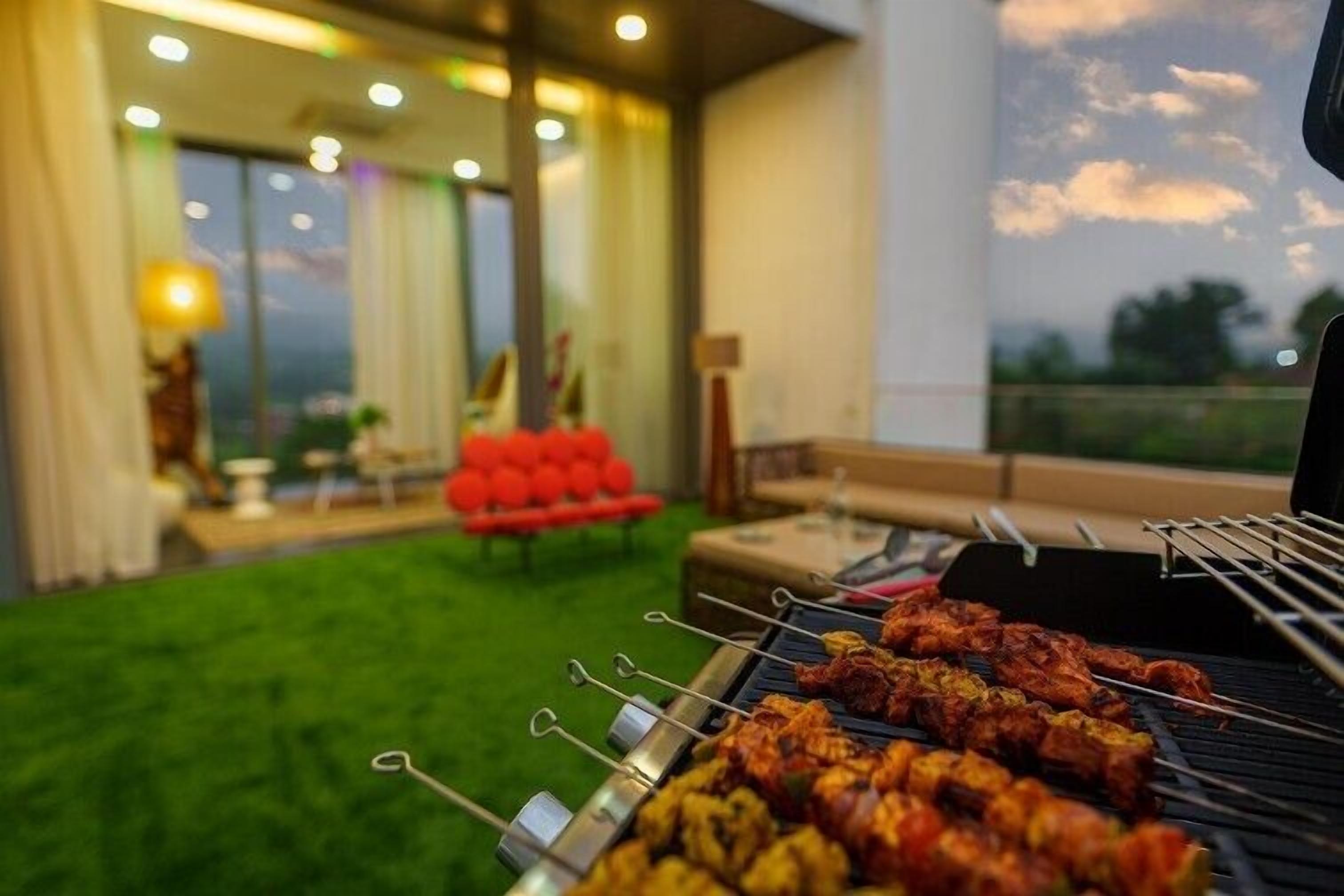 Un barbecue avec des brochettes de viande, un canapé rouge et une vue sur l’extérieur.