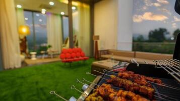 Un barbecue avec des brochettes de viande, un canapé rouge et une vue sur l’extérieur.