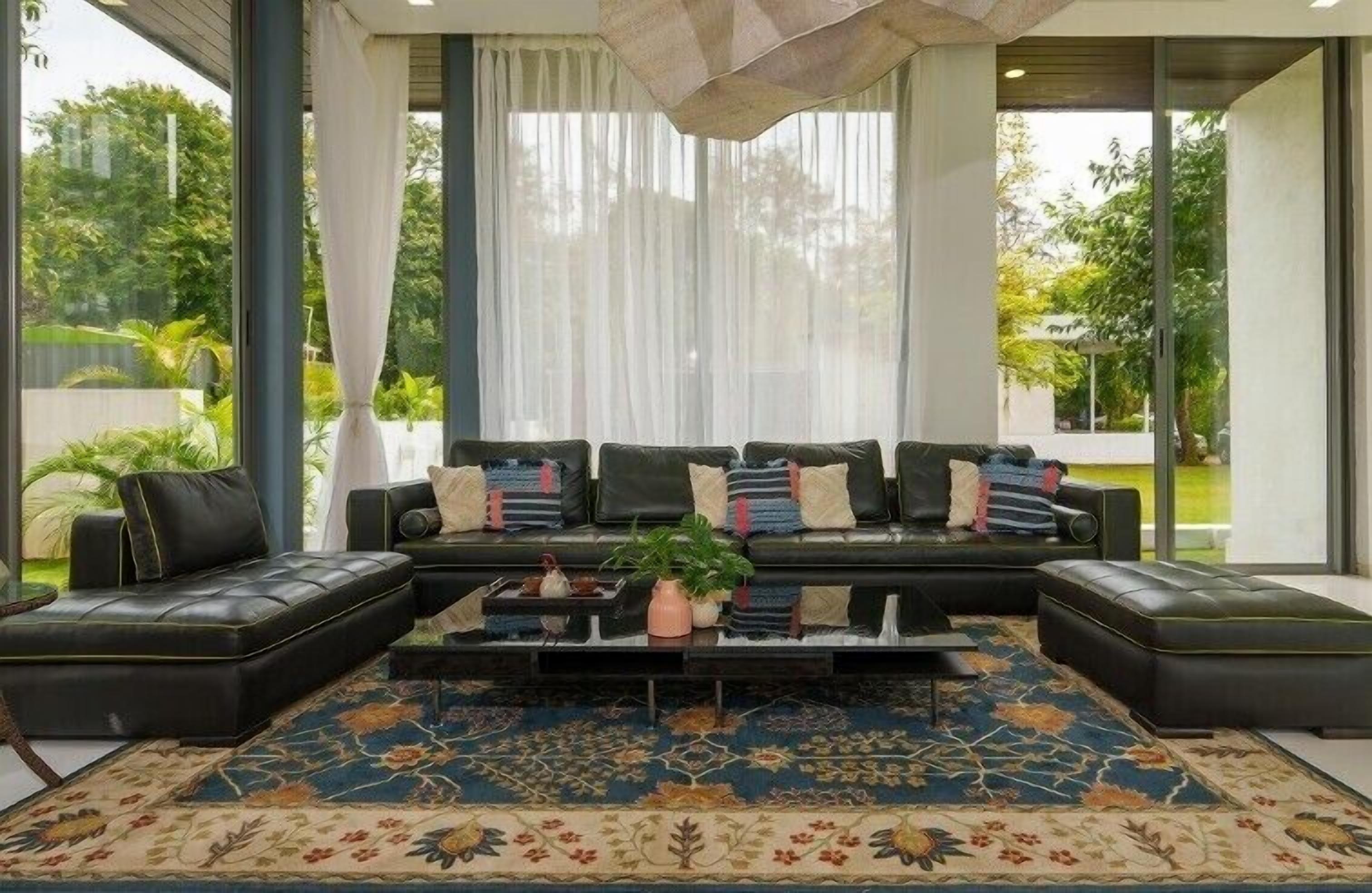 A modern living room with a black leather sofa set, a patterned rug, and a coffee table with a plant.