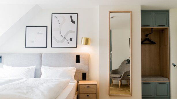 A modern bedroom with a bed, bedside tables, a wardrobe, and abstract wall art. - Bob W Munich Airport - Peterhof (Freising)