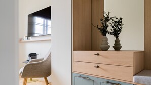 A modern room with a wooden cabinet, a grey chair, and a small table. - Bob W Munich Airport - Peterhof (Freising)