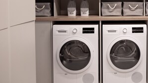 A laundry area with two Bosch washing machines, shelves with storage baskets, and a window with a view of greenery. - Bob W Munich Airport - Peterhof (Freising)
