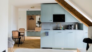 A compact kitchen with light blue cabinets, a black microwave, and a wooden ceiling beam. - Bob W Munich Airport - Peterhof (Freising)
