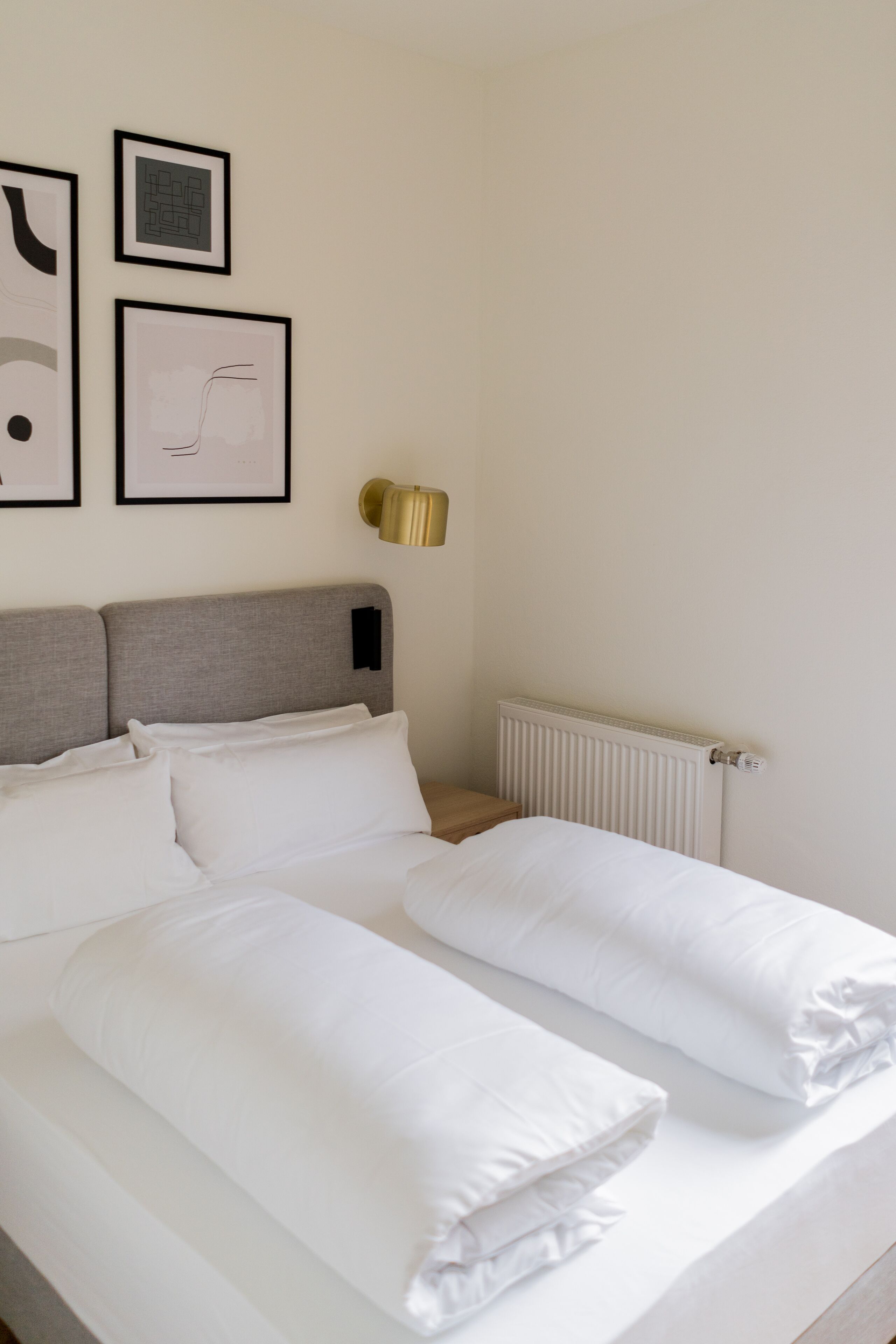 A neatly made bed with white linens and pillows, a headboard, and a wall-mounted lamp.