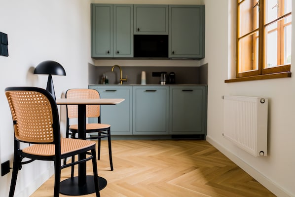 Una cocina moderna con armarios verde claro, suelo de madera en espiga y una zona de comedor con dos sillas y una mesa.