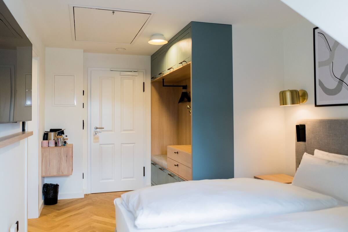 Une chambre d’hôtel comprenant un lit, une armoire, un bureau et une lampe fixée au mur.