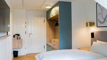 A hotel room with a bed, a wardrobe, a desk, and a wall-mounted lamp.