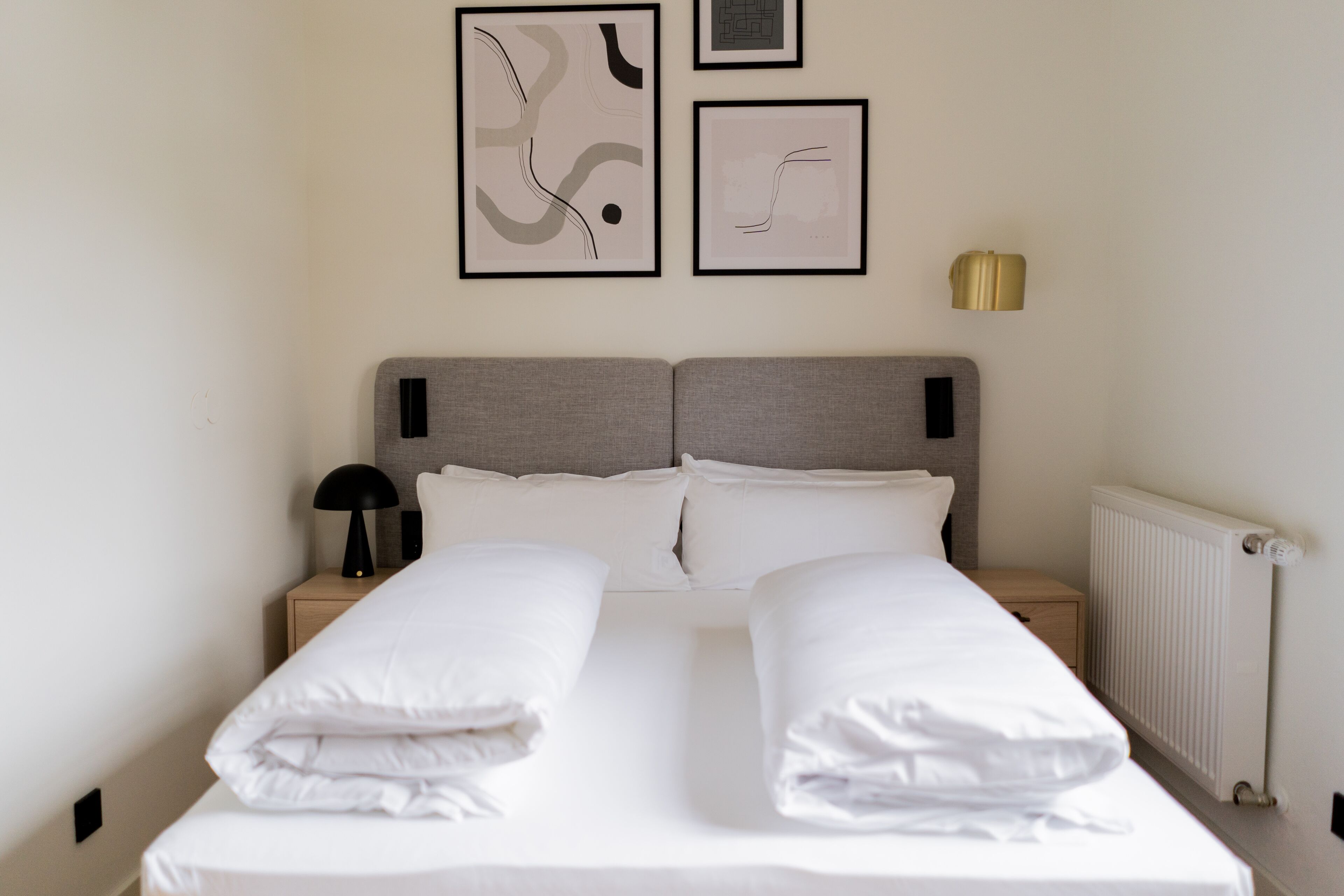 A neatly made bed with white linens, a grey headboard, and two bedside tables with lamps.