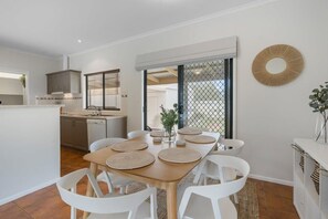 A modern kitchen with white cabinets, a dining table with white chairs, and a large window.