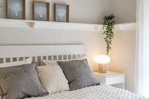 A neatly arranged bedroom with a bed, pillows, bedside table, lamp, and wall-mounted artwork.