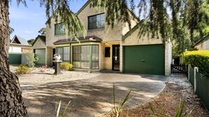 A two-story house with a driveway leading to a green garage, surrounded by trees and a gravel driveway. - The Black Door Bright, Victoria (Bright)