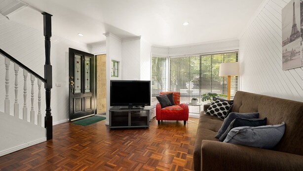 A modern living room with a wooden herringbone floor, a brown sofa with patterned cushions, a red armchair, and a flat-screen TV on a stand. - The Black Door Bright, Victoria (Bright)