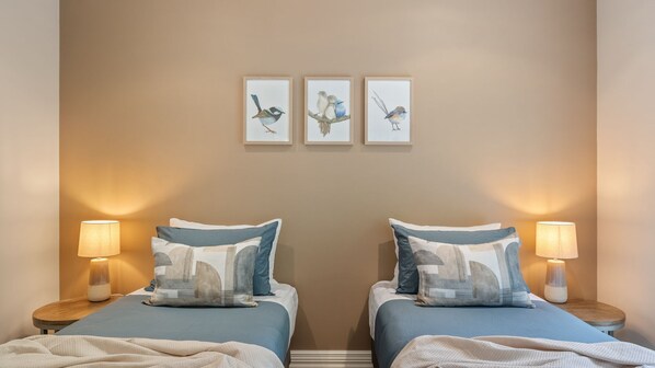Habitación de hotel con dos camas, cada una con una almohada y una lámpara de noche. Tres obras de arte enmarcadas decoran la pared sobre las camas.