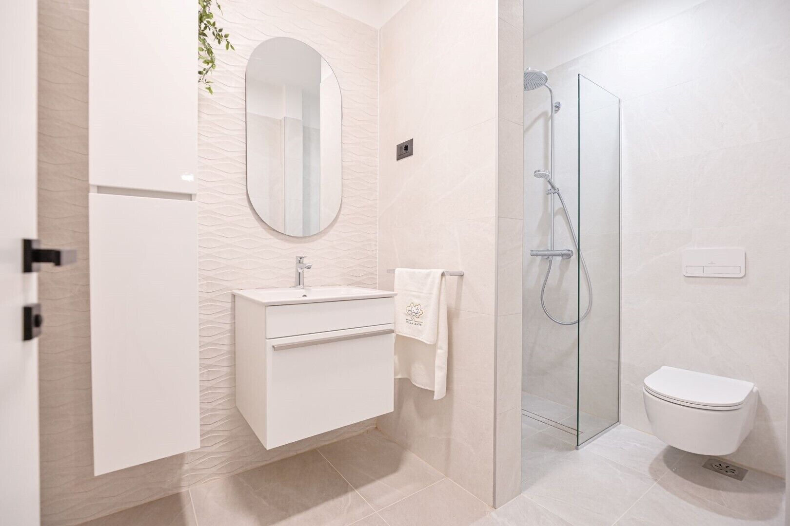 A modern bathroom with a white vanity, a round mirror, a glass shower enclosure, and a toilet.