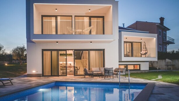 Une maison moderne à deux étages, dotée d’une piscine, d’un espace extérieur aménagé et d’un intérieur bien éclairé.