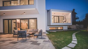 Une maison moderne dotée d’un patio aménagé avec du mobilier d’extérieur et une pelouse bien entretenue.