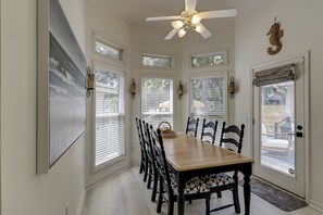 Un espace repas avec une longue table en bois, des chaises noires et un ventilateur de plafond.