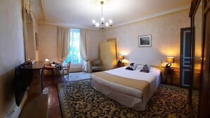 A hotel room with a large bed, a desk, a chair, a TV, and a chandelier. - Family chateau in the heart of an estate (Flacey)